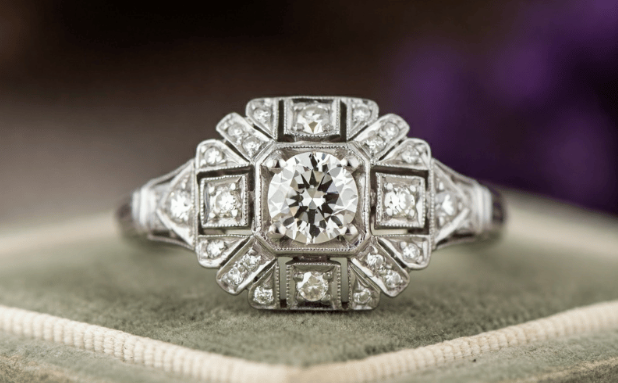 A close-up photo of a platinum 1930s ring with a central diamond surrounded by smaller diamonds in an elaborate geometric pattern.