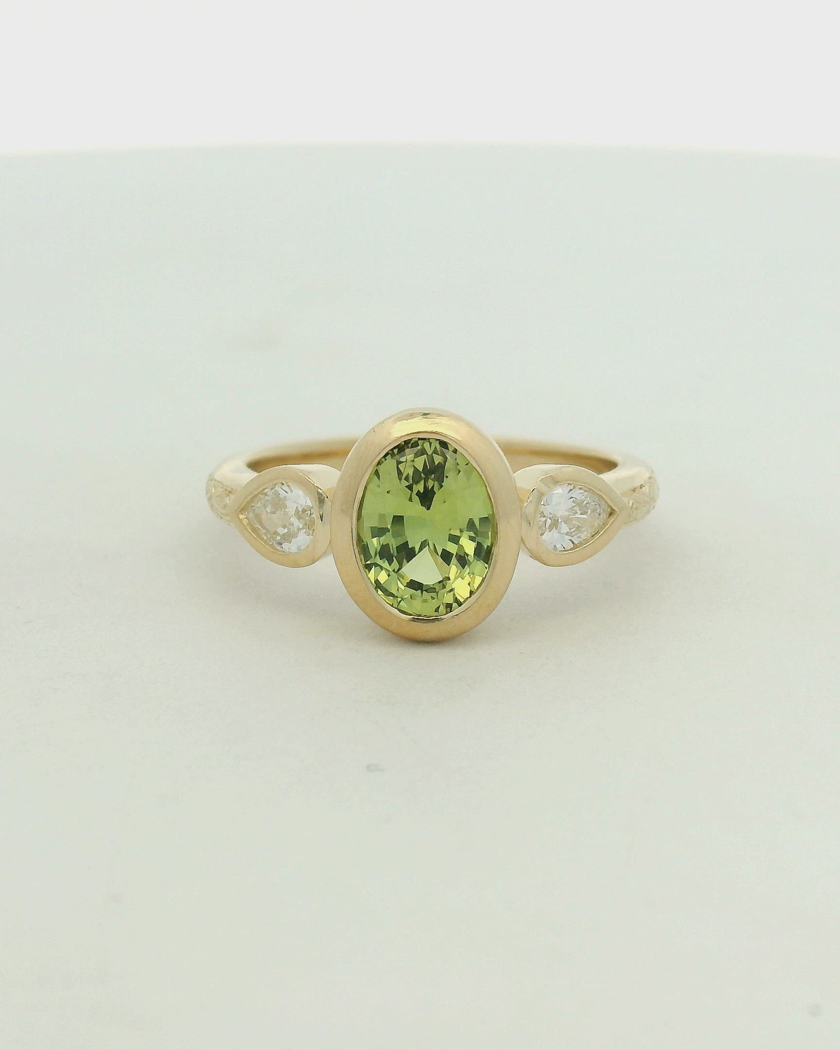 14k yellow gold oval green sapphire bezel set with pear lab diamond side stones and hand engraving engagement ring